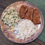 Picture of fried fish, rice, and coleslaw on a plate on a wooden table and blue/green placemat