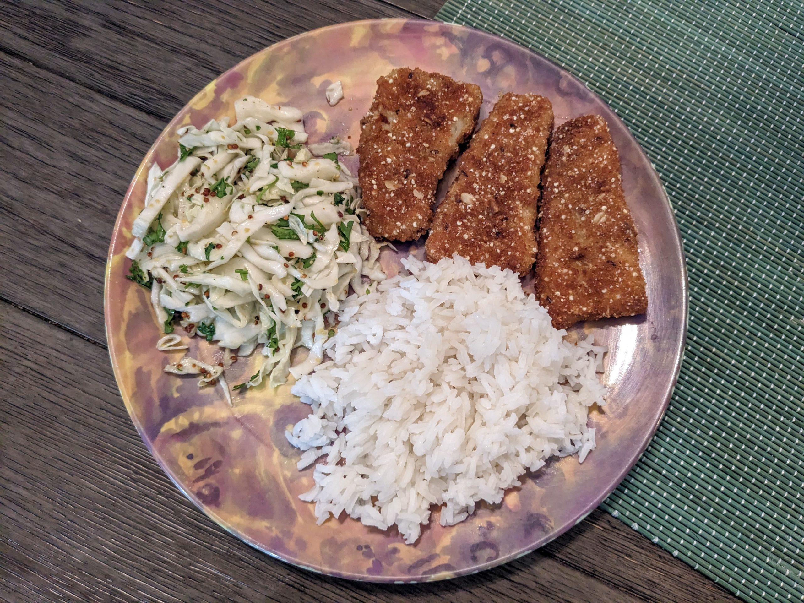 Picture of fried fish, rice, and coleslaw on a plate on a wooden table and blue/green placemat